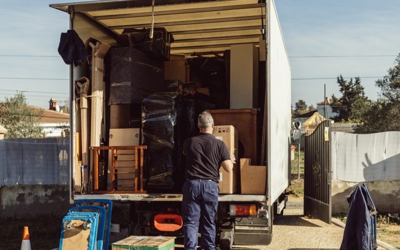Rear view of a older worker loading cardboard boxes onto moving truck